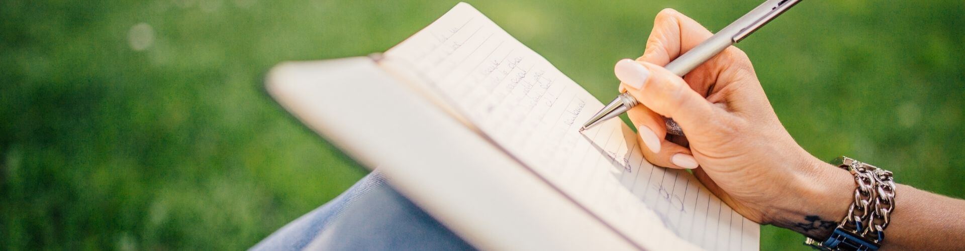 Person sat in nature writing in a branded notebook
